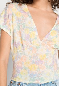 Blomstret bluse i blødt, let stof med et multicolor pastelmønster. Har en dyb V-hals og korte, capærmer.