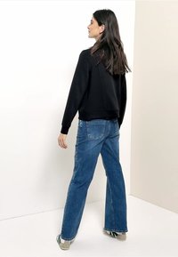 Sweat-shirt noir à col rond et poignets côtelés, associé à un jean évasé taille haute bleu clair et des chaussures en toile verte.