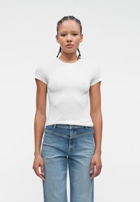 Biała koszulka z krótkim rękawem, okrągłym dekoltem, dopasowany krój, wykonana z gładkiej bawełny. Zestawiona z jasnoniebieskimi dżinsami, prosty fason.