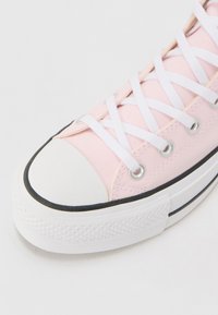 Rosa canvas sneakers med vita snören, en vit gummitåhette och en strukturerad vit sula med en svart accentlinje längs botten.