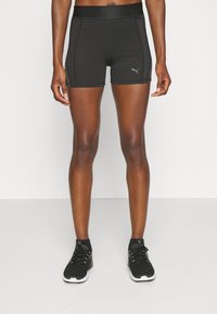 Pantalones cortos deportivos negros de material elástico, con una cinturilla alta y costuras de contraste, acompañados de zapatillas deportivas negras.