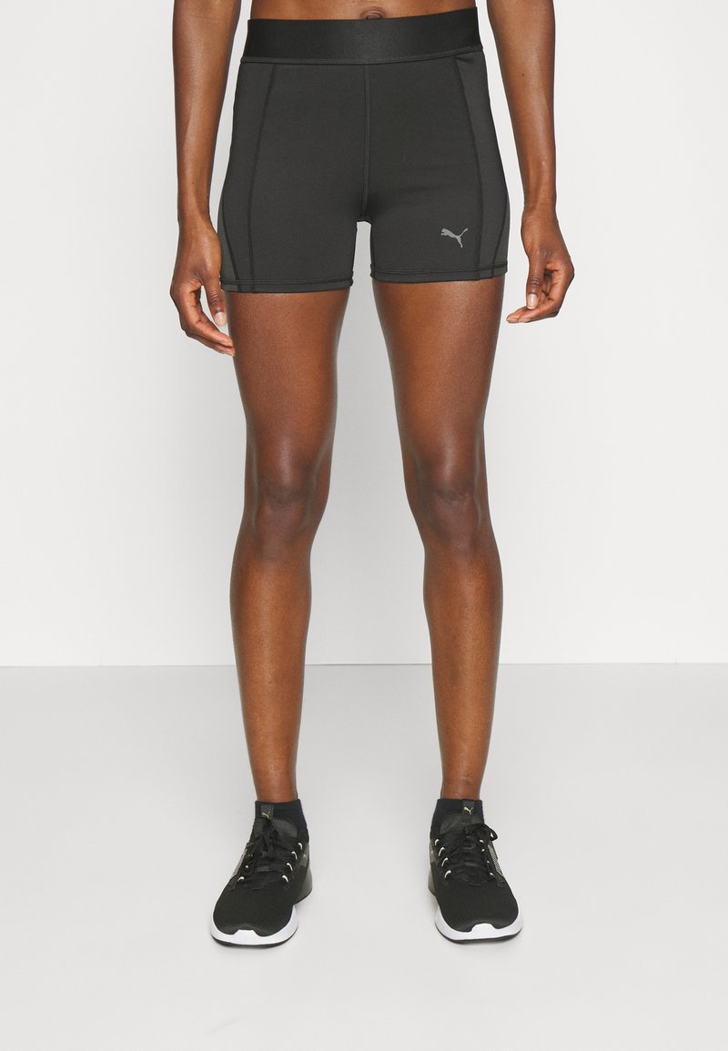Pantalones cortos deportivos negros de material elástico, con una cinturilla alta y costuras de contraste, acompañados de zapatillas deportivas negras.