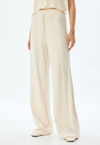 Lichtbeige wijde broek van een gestructureerde stof, met een elastische tailleband en trekkoord. Gladde, vloeiende uitstraling, volledige lengte.