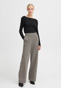 Must have musternik mustre pikkade varrukatega must top, millele on kombineeritud kõrge vöökoht ja laiad püksid, millel on pruuni ja beeži herringbone muster. Mustad kontsad.