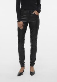 Zwarte neplederen broek met een slim fit, voorzakken en een gladde textuur, gecombineerd met puntige zwarte hakken.