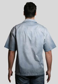 Camicia a maniche corte, di colore azzurro chiaro, con una texture morbida e un fit rilassato. Presenta un yoke posteriore e un orlo dritto. Indossata su jeans scuri.