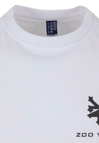Hvid bomulds T-shirt med rund hals, der har et stort sort grafisk design på forsiden og brandnavnet "ZOO YORK" nedenfor.