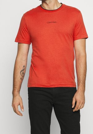 Rød bomulds t-shirt med korte ærmer og rund halsudskæring, med et sort Calvin Klein-logo på brystet. Glat tekstur.