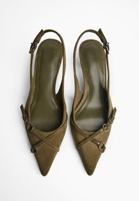 Scarpe slingback in suede marrone con punte appuntite, dotate di fascette incrociate e dettagli metallici. Le solette sono di un verde scuro con dettagli di cucitura.