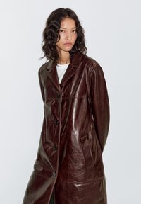 Bruine leren jas met een glanzende afwerking, voorzien van een kraag, knopen aan de voorkant en zijzakken, met een rechte, ontspannen pasvorm.
