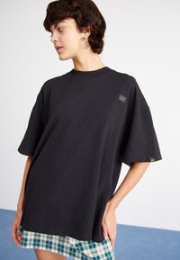 Camiseta negra de gran tamaño con cuello redondo y mangas cortas. Presenta un parche de logo texturizado en el pecho y una tela de algodón suave.