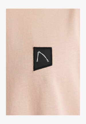 Material de bumbac roz deschis, cu un patch rectangular negru cu linii albe. Patch-ul este coase cu margini vizibile.