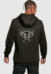 Sudadera negra con un diseño de dos calaveras con alas y el texto "DEMON INSIDE" en la parte de atrás. Textura suave con puños acanalados.