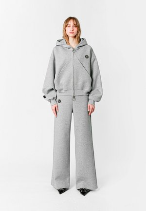 Sudadera gris con capucha y cremallera plateada. Combinada con pantalones de chándal grises de pierna ancha. Ambos tienen una textura suave y acentos de logo.