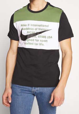 Kurzärmliges T-Shirt mit Blockfarben in Schwarz, Grün und Weiß; großer schwarzer Nike-Swoosh; gedruckter Text in Grün. Aus Baumwolle.