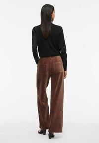 Pantalons en velours côtelé marron à jambes larges avec une texture douce, dotés de deux poches arrière. Associés à un haut noir à manches longues et des chaussures à talons.