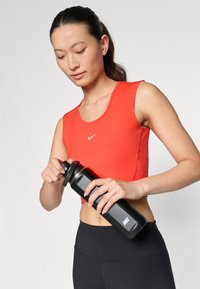 Rød crop top med rund hals, kombinert med svarte leggings. Personen holder en svart Nike vannflaske med skrukork.