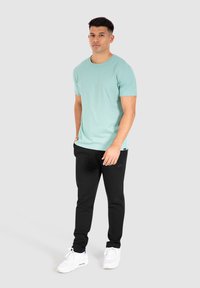 Lichtgroene katoenen T-shirt met een ronde hals, gecombineerd met zwarte sweatpants. De outfit heeft een minimalistisch ontwerp en een relaxte pasvorm.