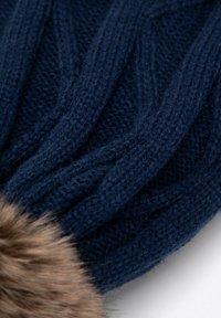 Pletená tmavě modrá čepice s copánkovým vzorem, zdobená měkkým hnědým umělým kožíškem na základně. Texturovaná látka poskytuje teplo.