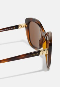 Ochelari de soare cu scoică țestoasă și lentile maro, având accente aurii pe brațe și branding "vogue". Formă clasică pătrată cu detalii decorative.