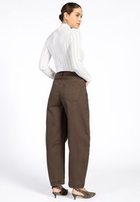 Bruine hoog-waist broeken met een losse pasvorm, gecombineerd met een ribbelige witte top. Kenmerkende zakken en schoenen met een luipaardprint accentueren de outfit.