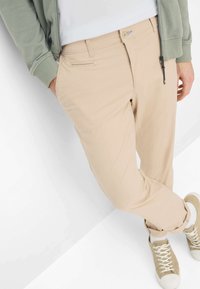 Beige chino's met een slim fit, van katoen, ritssluiting, voorzakken en een achterste paspelzak. Gecombineerd met beige sneakers en een lichtgroene jas.