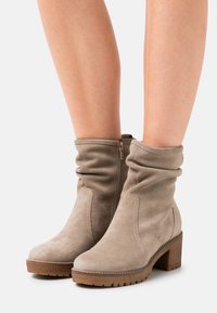 Beige Wildleder-Stiefeletten mit einem lässigen Design, seitlichem Reißverschluss und einem klobigen braunen Absatz, mit genähten Akzenten und einer strukturierten Laufsohle.