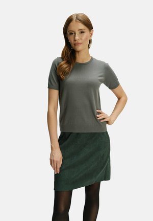 Top gris de manga corta con un diseño ajustado y cuello de canalé, combinado con una falda de ante verde oscuro y medias negras.