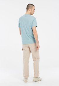 Svetlomodré tričko s krátkym rukávom vyrobené z bavlny, kombinované s béžovými cargo nohavicami a svetlými teniskami. Viditeľné švy a voľný strih.