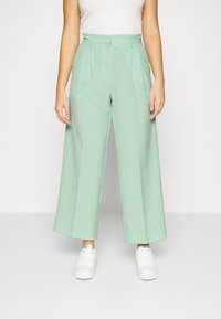 Pantalons à jambes larges mint en tissu lisse, avec des plis à l'avant et une taille ajustée, associés à des baskets blanches.