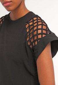 Top nero con maniche corte e un design a trame intrecciate sulle spalle. Tessuto liscio con una morbida texture e una vestibilità comoda.