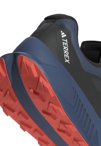 Scarpa atletica blu e nera con parte superiore testurizzata, dotata di una suola in gomma rossa con profondi motivi di trazione e il marchio "Terrex".