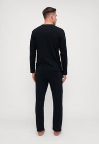Schwarzes Langarmoberteil und passende Jogginghose, beide aus glattem Material. Merkmale einen runden Halsausschnitt und eine lockere Passform. Durchgehend einfarbig.