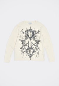 Κρεμ μακρυμάνικο πουκάμισο με μαύρο συμμετρικό αφηρημένο γραφικό που μοιάζει με ασπίδα και αγκάθια στο μπροστινό μέρος.