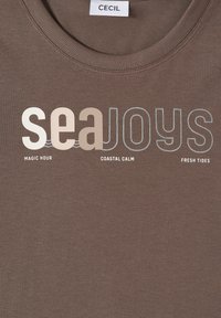T-shirt en coton marron à col rond, avec le texte « seaJoys » en blanc et beige clair, et un texte additionnel en dessous en bleu clair.