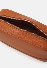 Brown leather cosmetic bag with a textured surface, gold zipper closure, and a simple rounded shape. Interior label visible.