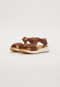 Sandales en cuir marron avec des sangles croisées, une semelle intérieure rembourrée et une semelle texturée. Présentent un léger talon et une sangle ajustable.