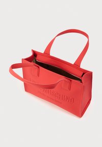 Κόκκινη συνθετική τσάντα ώμου με ανάγλυφο λογότυπο, δύο λαβές και ανοιχτό πάνω μέρος με εσωτερική τσέπη με φερμουάρ. Ομαλή υφή.