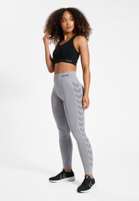 Czarny stanik sportowy i jasnoszare legginsy w wzór rybiej ości, wysoki stan, elastyczny materiał, w połączeniu z czarnymi butami sportowymi.