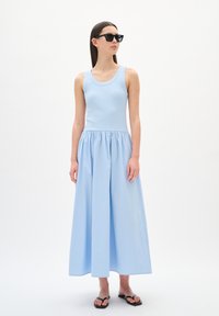 Haut sans manches bleu clair avec une texture côtelée, associé à une longue jupe fluide bleu clair avec une taille élastique. Le mannequin porte des lunettes de soleil noires.