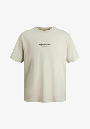 T-shirt en coton de couleur beige clair avec des manches courtes et un logo sur la poitrine, associée à un pantalon cargo noir et des baskets noires avec des semelles blanches.