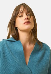 Blåstickad kofta med ribbat mönster, bred krage och djup V-ringning, tillverkad av mjukt, lätt material.