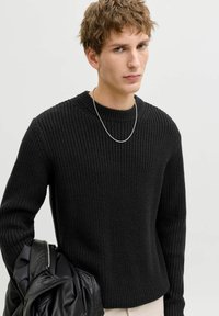 Czarny sweter z dzianiny o fakturowanym wzorze, okrągły dekolt, prążkowane mankiety i luźny krój; noszony z czarną skórzaną kurtką.