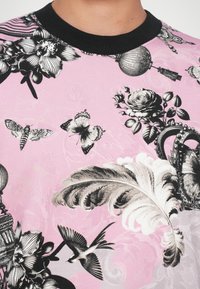 Camicia di stoffa rosa con motivi floreali e farfalle neri, caratterizzata da un colletto a costine nero e dettagli intricati come serpentelli e uccelli.