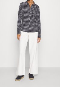 Navy button-up shirt with white geometric print, long sleeves, and a collar, paired with white flared pants and black ankle boots.