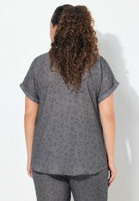 Top grigio a maniche corte con un sottile motivo leopardato, vestibilità ampia, polsini arrotolati e orlo leggermente curvo. La texture sembra leggera e morbida.