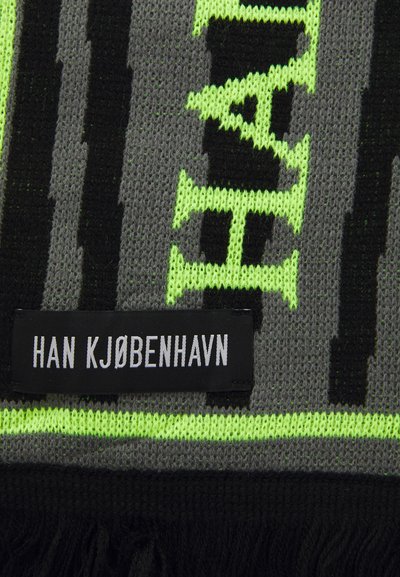 Close-up de tecido de malha com listras cinzas, pretas e verde neon e texto, apresentando uma etiqueta preta com a inscrição "HAN KJØBENHAVN" em branco.