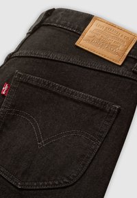 Jeans in denim scuro con un'etichetta in pelle, tasca posteriore visibile con cuciture distintive e un accento di etichetta rossa sulla cucitura sinistra.