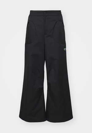 Schwarze weit geschnittene Hose aus glattem Material mit großen Vorder-Taschen und einem subtilen Akzent an der Seite. Standard Knopfverschluss an der Taille.