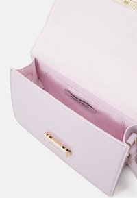 Jasnofioletowa torebka o gładkiej fakturze, z zapięciem z złotego metalu i metką wewnątrz. Wnętrze wyłożone różową tkaniną.